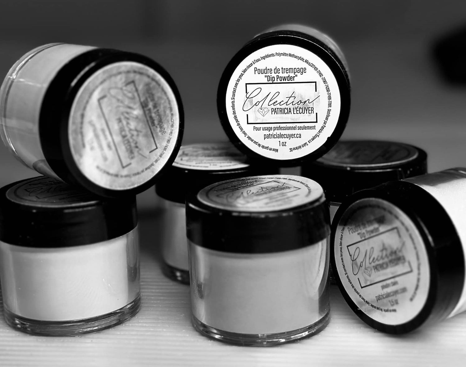 Pots de poudre de trempage pour ongles de la Collection Patricia L’Écuyer. Petits contenants transparents avec couvercles noirs, étiquettes visibles indiquant “Dip Powder – Pour usage professionnel seulement – patricialecuyer.ca